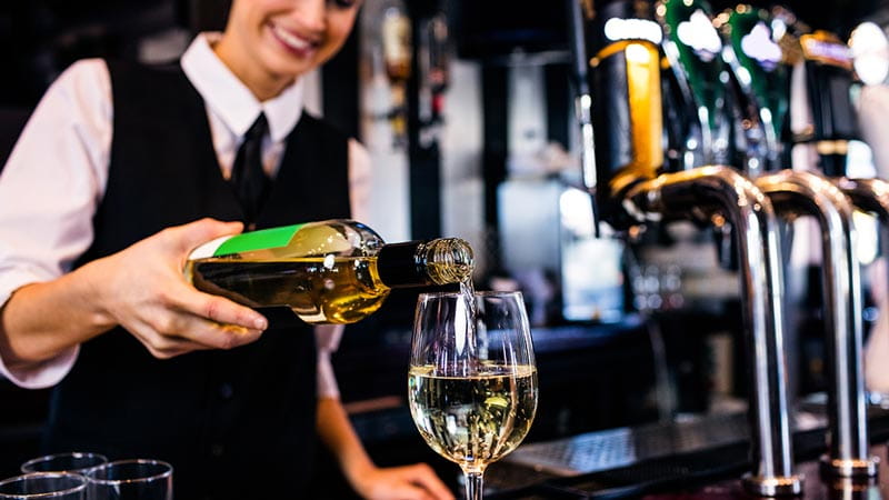 Bar – Frau schenkt sich ein Glas Weißwein an der Bar ein